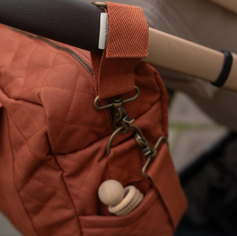Red quilted bag with a strap and pacifier attached, possibly in a car seat.