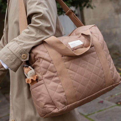 Person holding a quilted beige handbag with a brand label, wearing a beige coat.