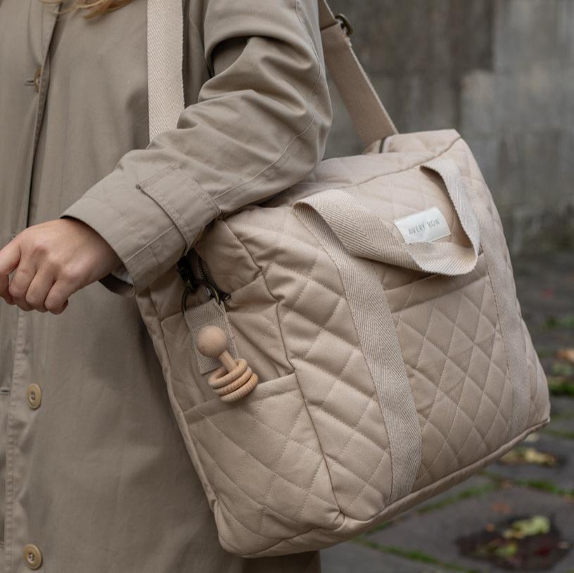 Person holding a beige quilted bag with a visible brand label, wearing a matching coat.