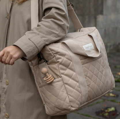 Person holding a beige quilted bag with a visible brand label, wearing a matching coat.