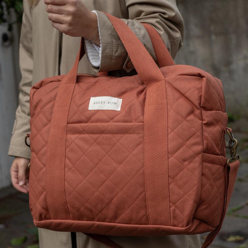 Person holding a quilted orange bag with a visible brand label against a blurred background