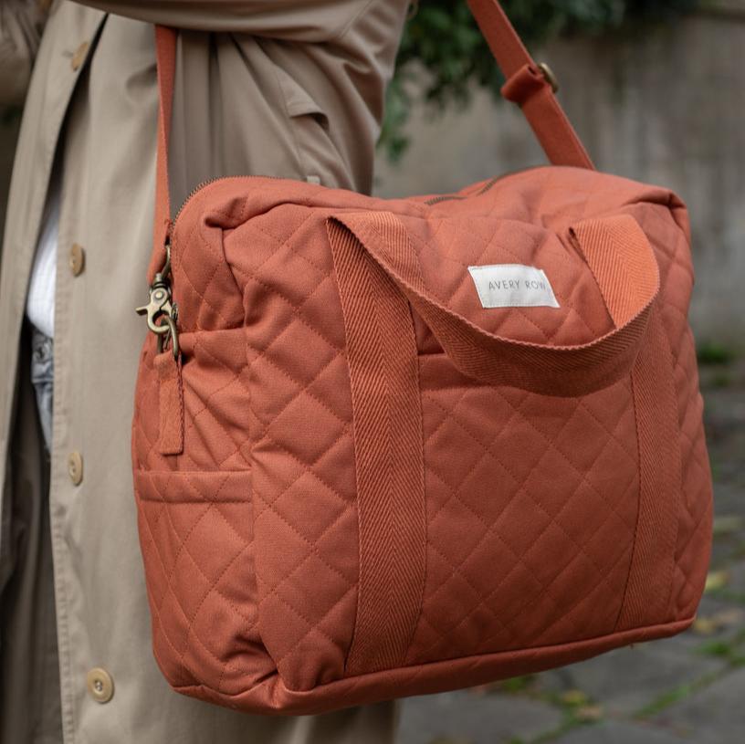 Quilted orange bag held by a person wearing a beige coat.