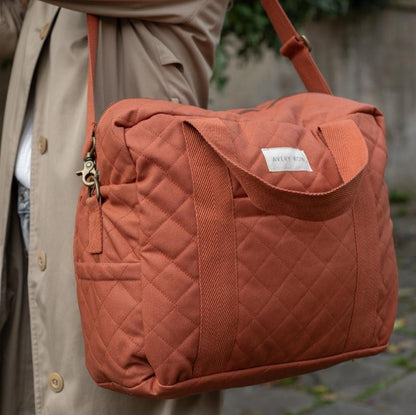 Quilted orange bag held by a person wearing a beige coat.