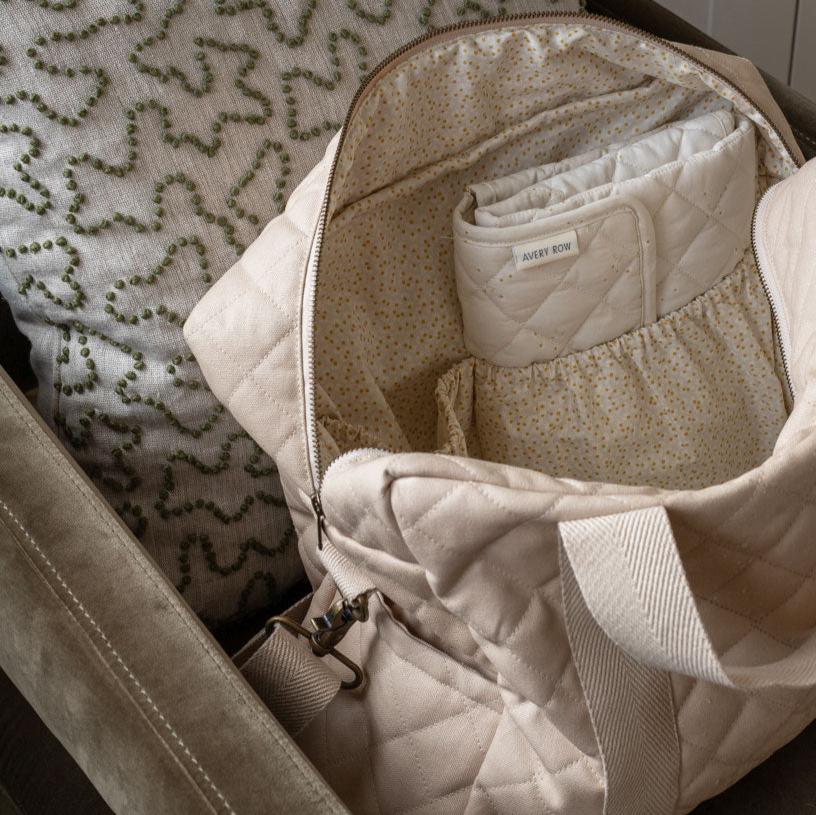 Beige quilted bag with a folded baby blanket inside, on a textured surface.