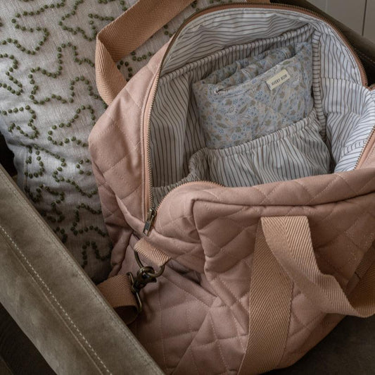Quilted pink bag with baby clothes inside, on a textured surface.