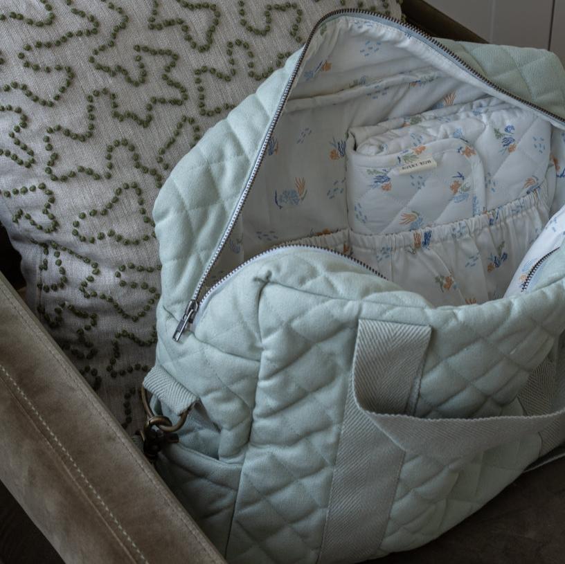 Light blue quilted baby bag with baby clothes on a patterned surface