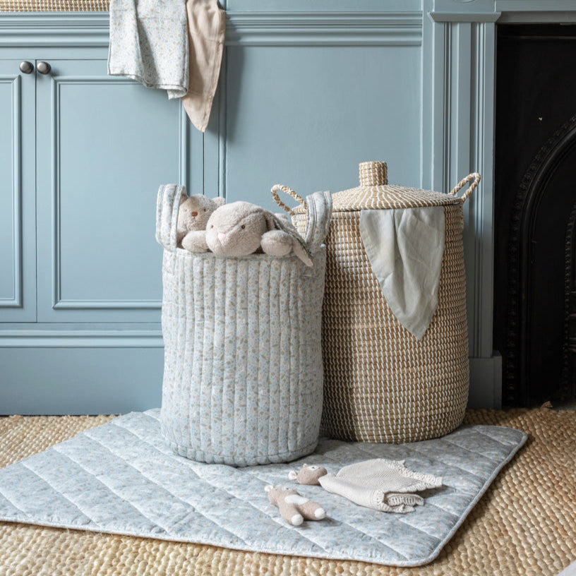 Two woven baskets with toys on a rug in a room with blue walls and a fireplace.