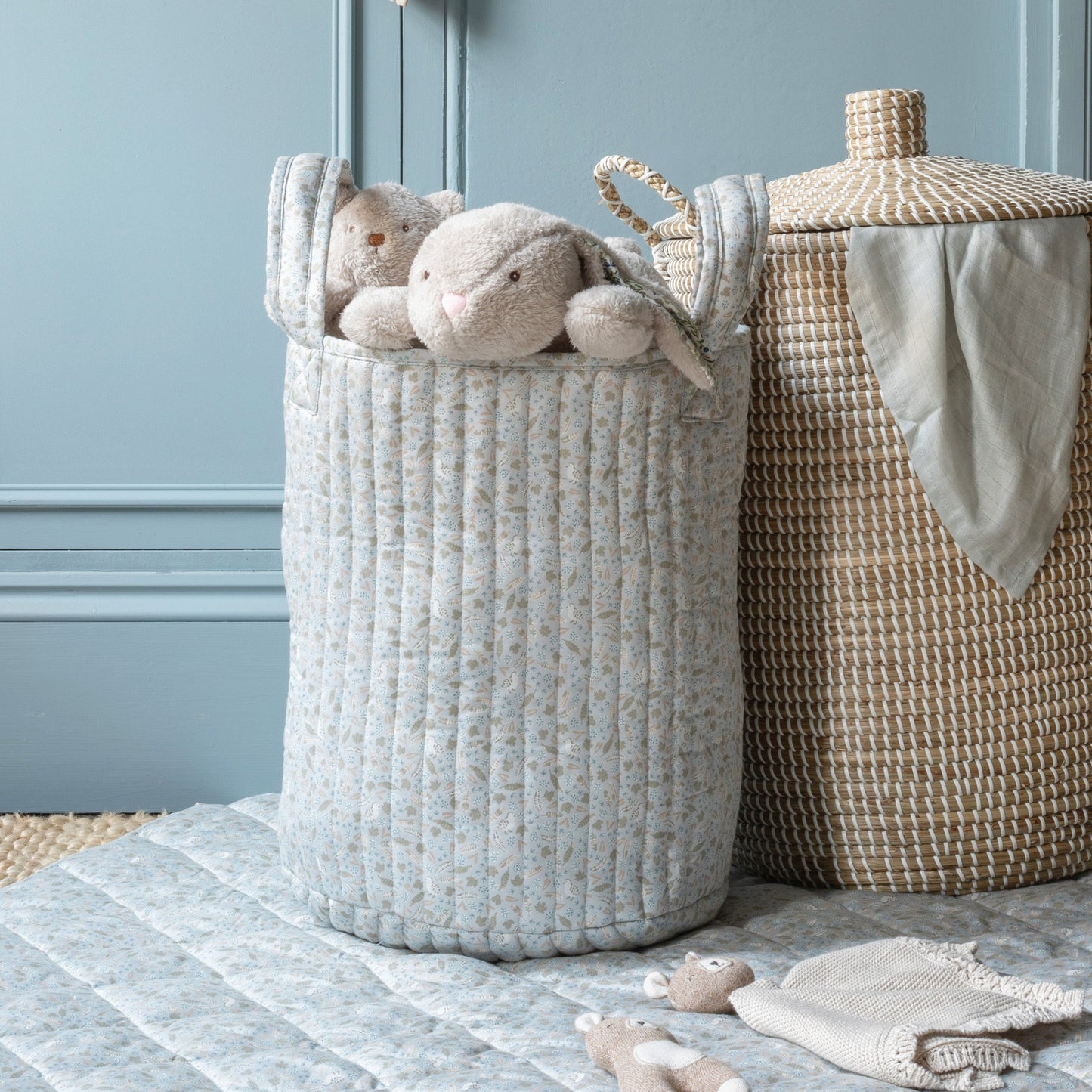 Woven laundry basket with plush toys and a towel against a light blue wall.