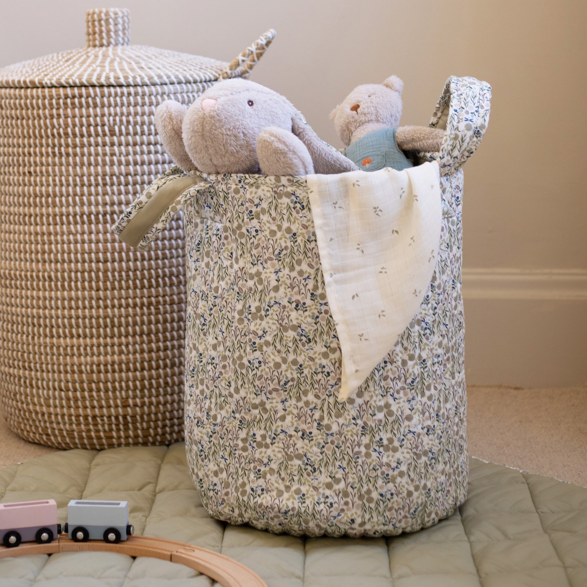 Floral-patterned storage basket with toys on a bed