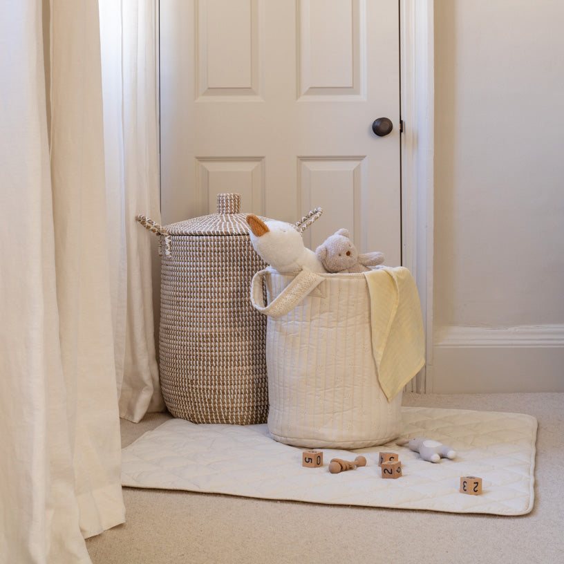 White laundry basket with toys on a white rug next to a white door.