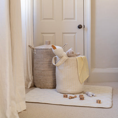 White laundry basket with toys on a white rug next to a white door.
