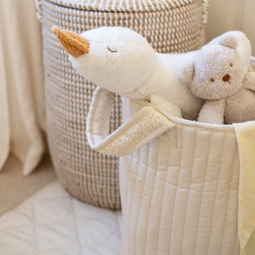 Plush swan and bear toys in a quilted basket with a textured wall in the background