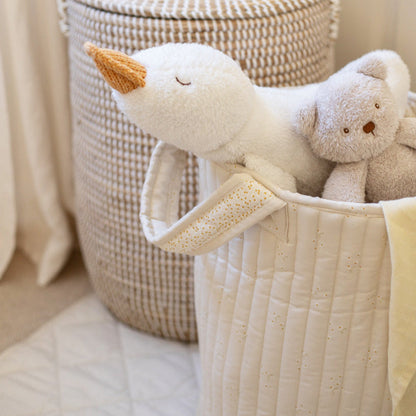 Plush swan and bear toys in a quilted basket with a textured wall in the background