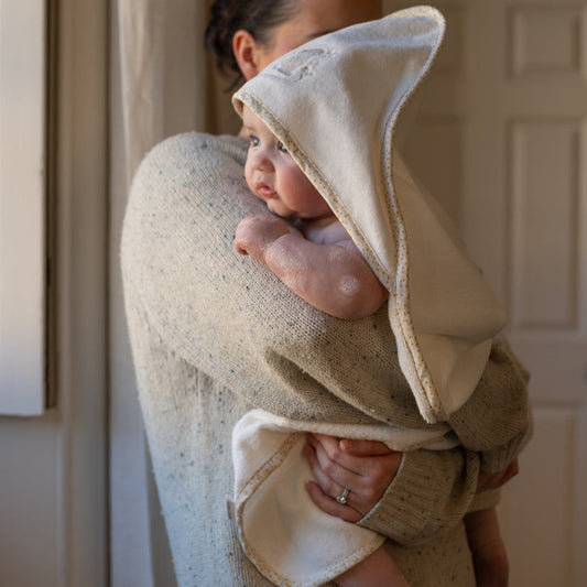 Baby wrapped in a beige hooded blanket being held by an adult.