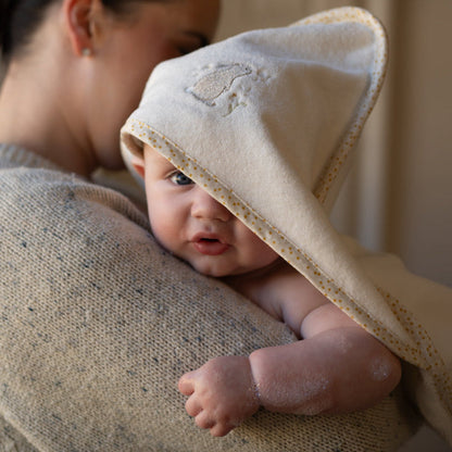 Baby wrapped in a beige hooded towel being held by a person