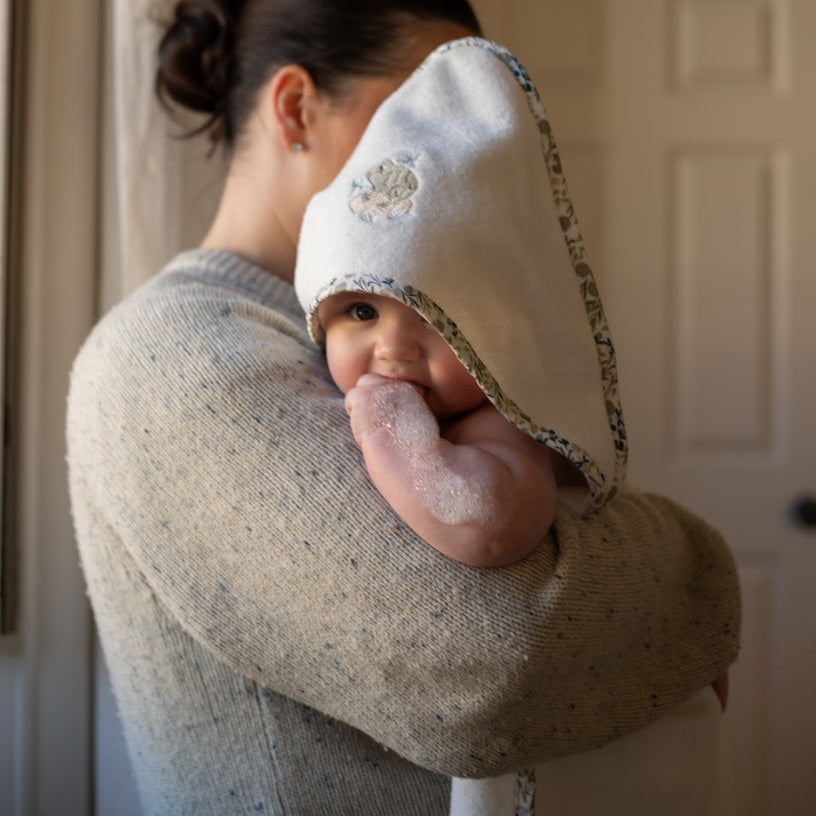 Person holding a baby wearing a white hooded blanket with floral trim.