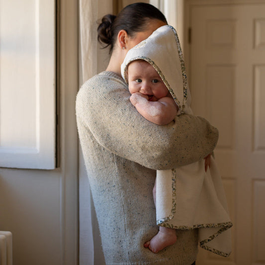 Woman holding a baby wrapped in a towel in a room with neutral walls.
