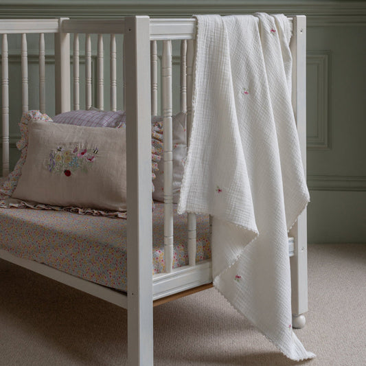 White crib with floral bedding and a white blanket in a nursery setting