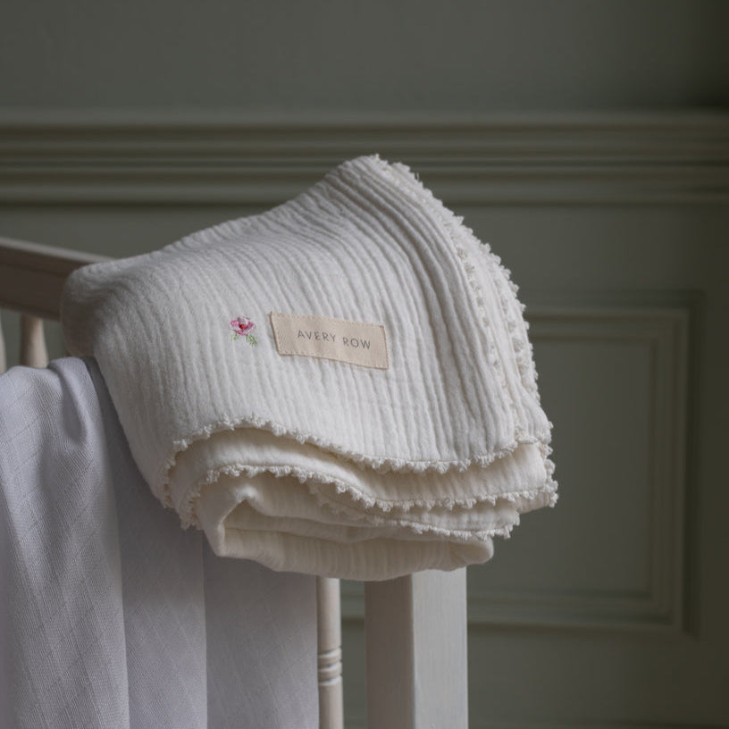 Folded white textured blanket with a label on a wooden stand against a neutral wall.
