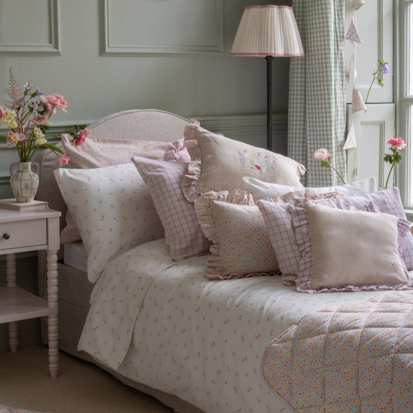 Bedroom with a bed covered in patterned bedding and pillows, next to a nightstand with flowers.