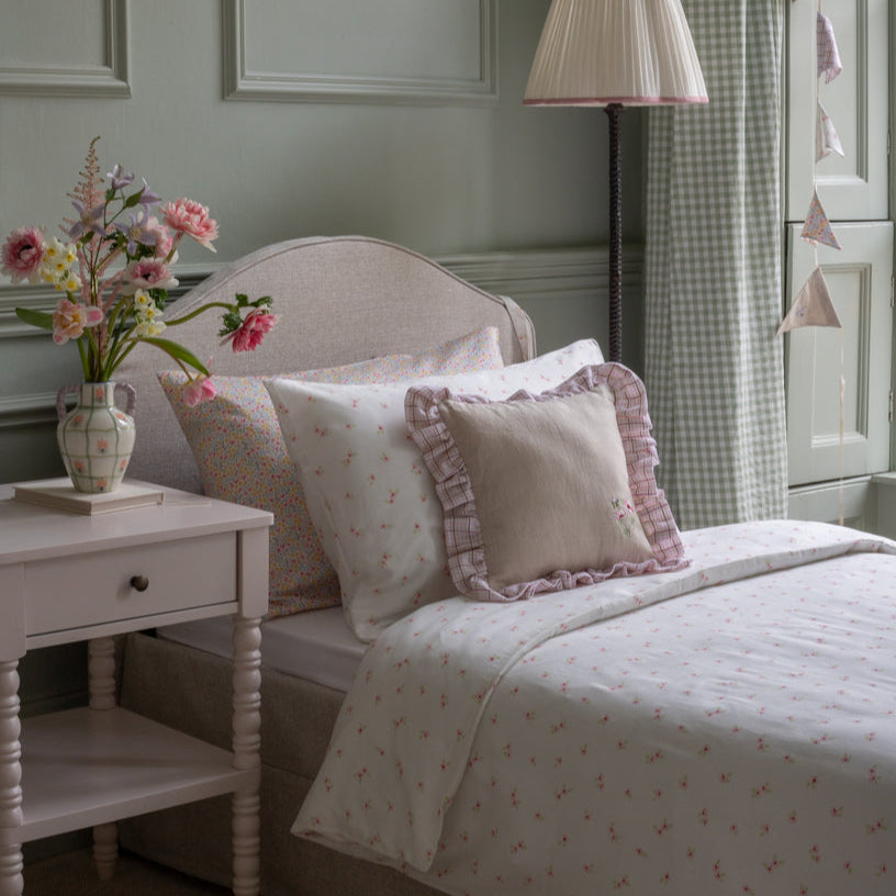 Bedroom with a bed featuring patterned bedding and pillows, a nightstand with flowers, and a lamp.