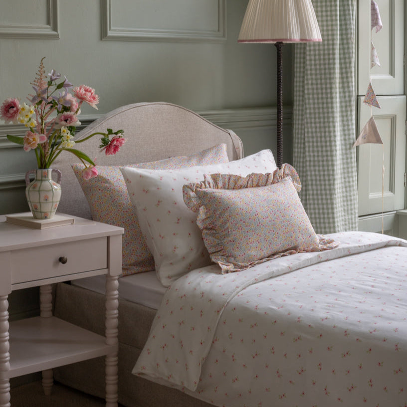 Bedroom with floral bedding, pillows, and a side table with flowers.