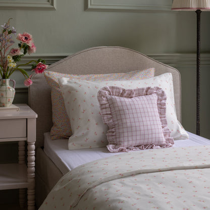 Bed with patterned pillows and a side table with flowers in a bedroom setting