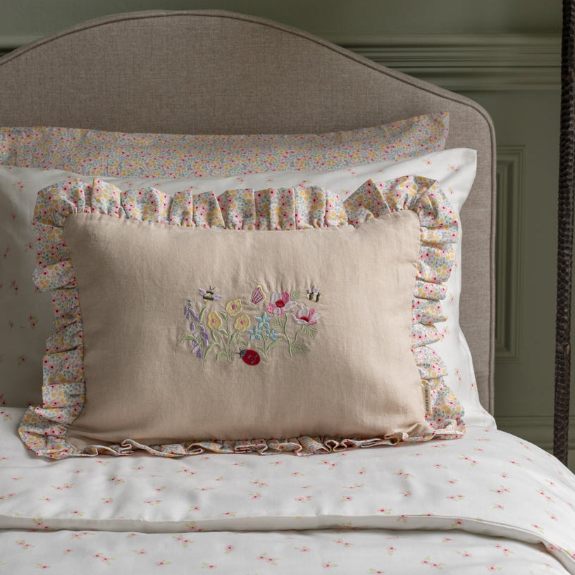Decorative pillow with floral embroidery and ruffled edge on a bed with matching bedding.
