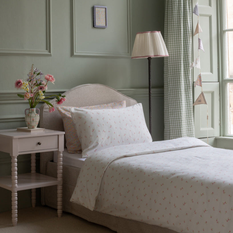 Neatly made bed with floral arrangement and lamp in a bedroom setting
