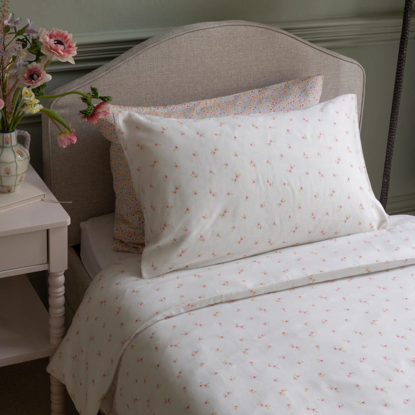 Floral patterned bedding set on a bed with a side table and flowers.