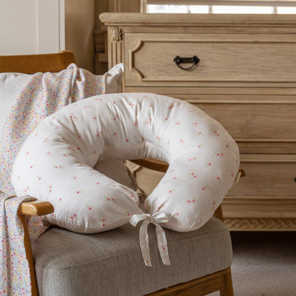 White baby boppy pillow with pink patterns on a chair in a bedroom setting