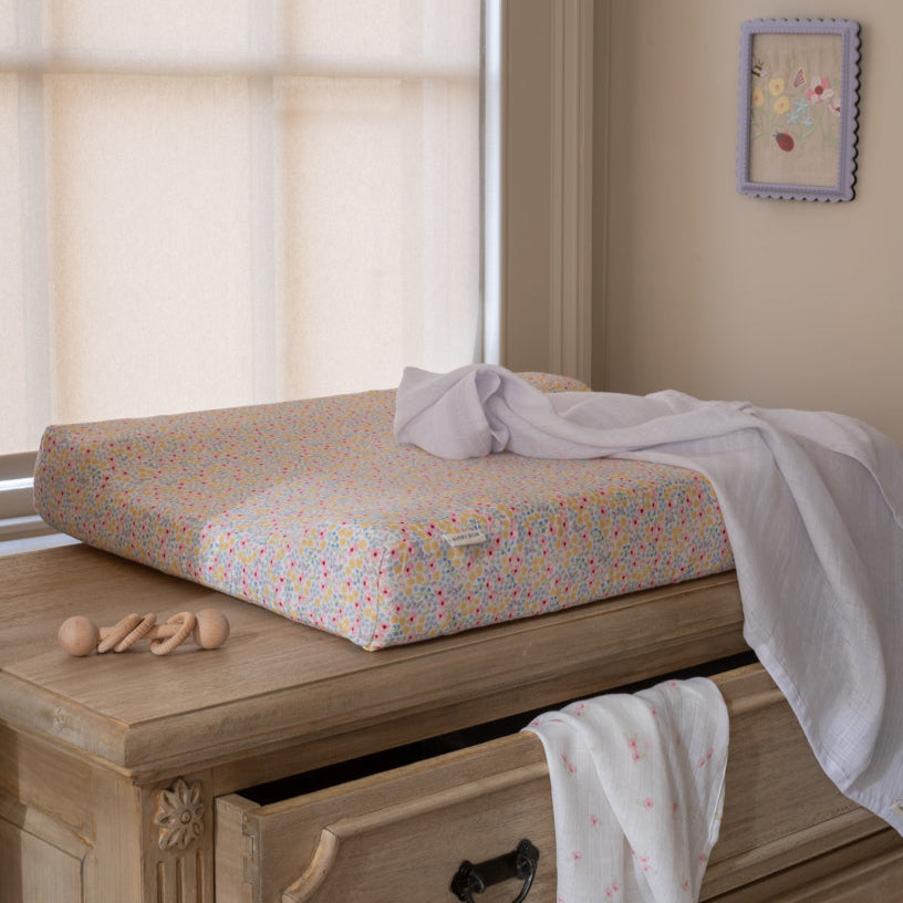 Floral-patterned changing pad on a wooden dresser with toys and a towel.