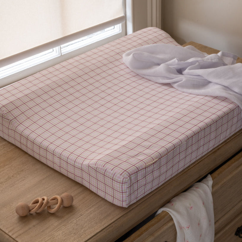 Grid-patterned mattress cover on a wooden bed with toys and clothes in the background
