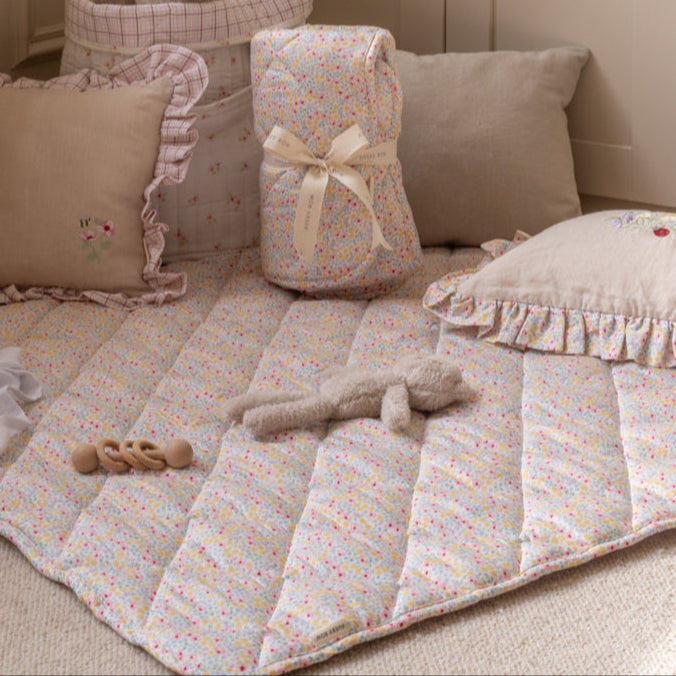 Baby crib with floral bedding, pillows, and a toy on a beige carpet.