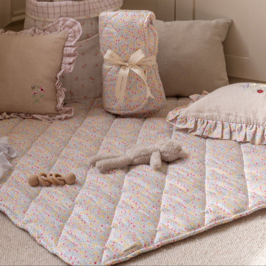 Baby crib with floral bedding, pillows, and a toy on a beige carpet.