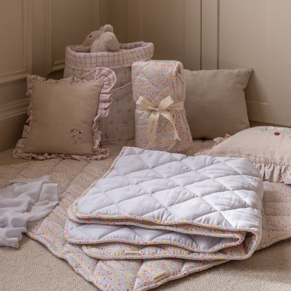 Stack of floral-patterned quilts on a bed with pillows and a teddy bear in the background.