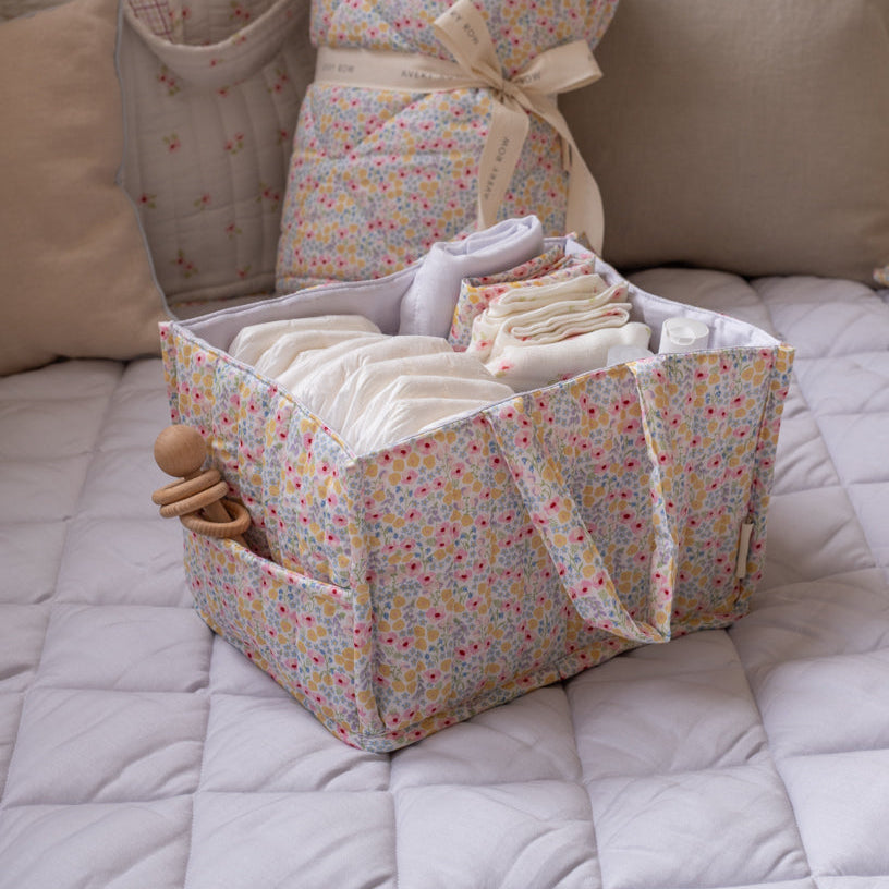 Floral-patterned baby organizer with diapers and a toy on a bed