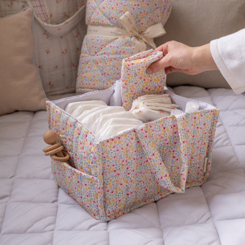 Floral-patterned baby organizer with diapers and a toy on a bed