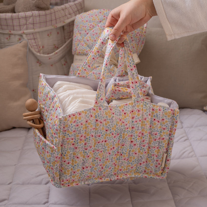 Floral-patterned diaper bag with baby items on a bed