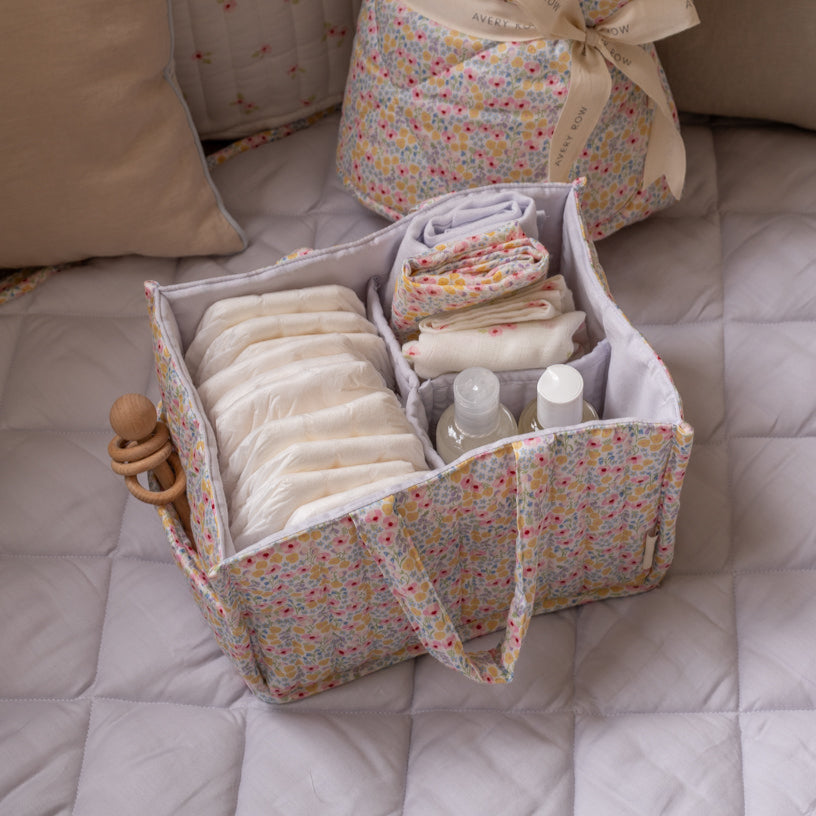 Baby essentials in a floral storage bag on a bed