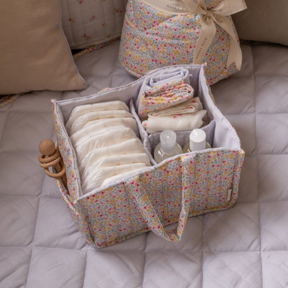 Baby essentials in a floral storage bag on a bed