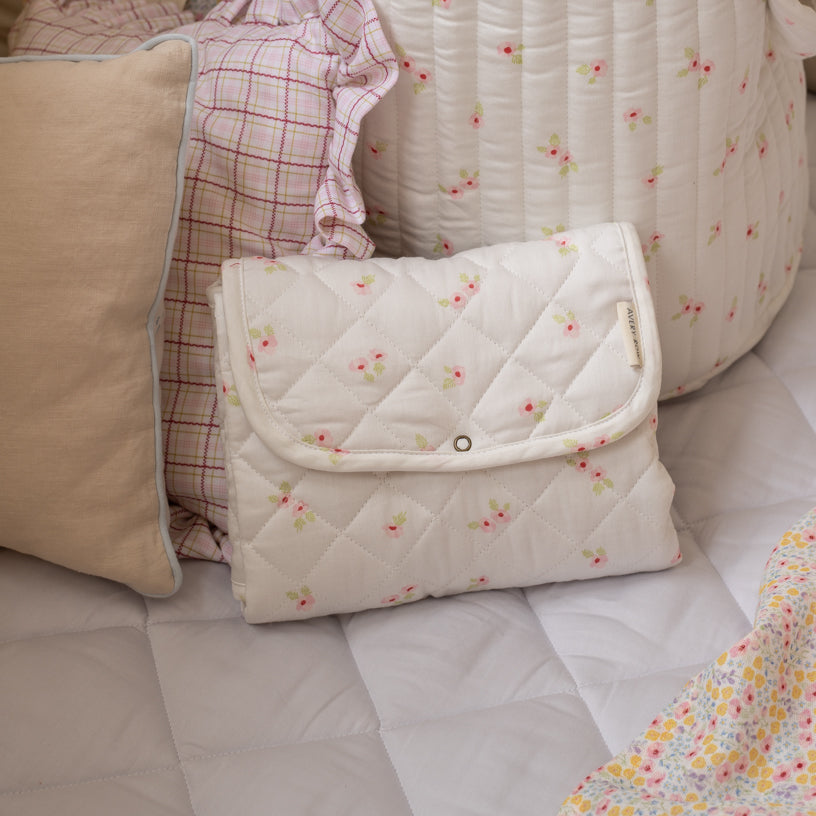 Quilted baby blanket with floral pattern on a bed with pillows and blankets.