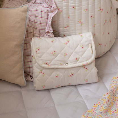 Quilted baby blanket with floral pattern on a bed with pillows and blankets.