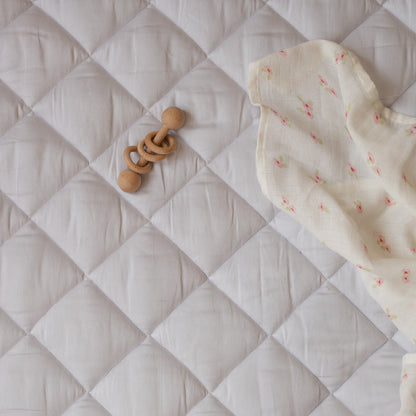 Wooden baby rattle and soft fabric on a quilted surface