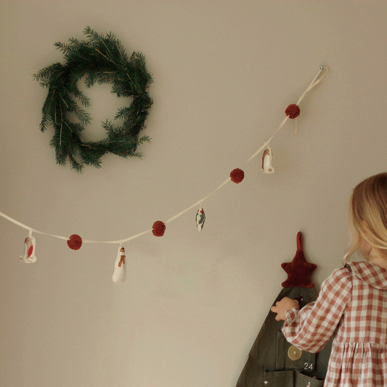 Person decorating a wall with a wreath and festive garland on a neutral background