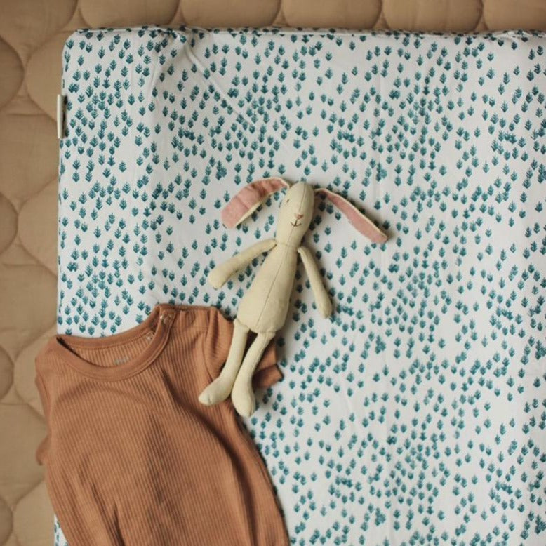 Baby outfit and plush toy on a crib with a patterned sheet