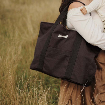Person holding a black bag with a child in a field