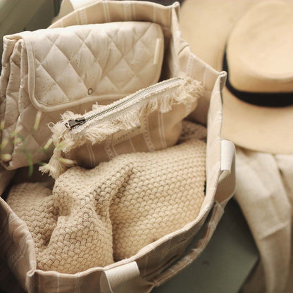 Close-up of a beige textured bag with a hat and folded fabric in the background