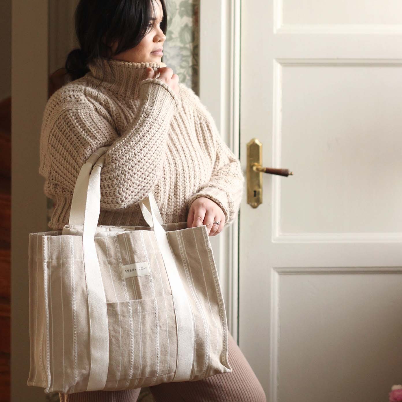 Woman holding a large striped tote bag in front of a white door.