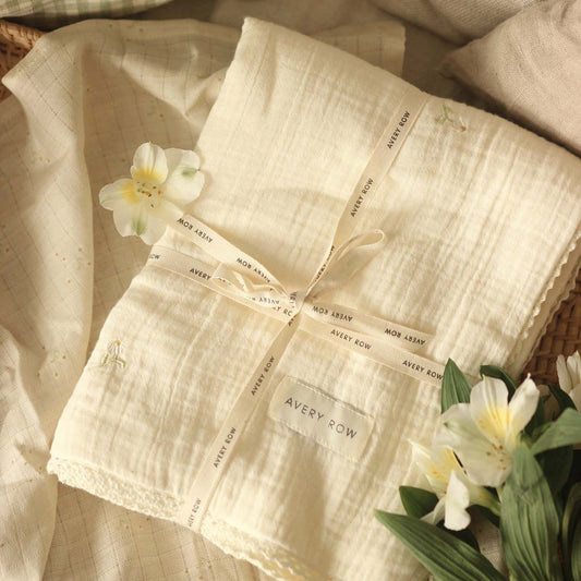 Beige fabric with 'Avery Row' branding, tied with a ribbon, surrounded by white flowers.